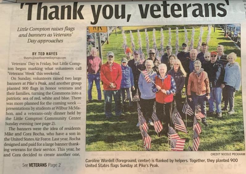 Photo of a newspaper article headlined "Thank you, veterans: Little Compton raises flags and banners as Veterans Day approaches." Photo of volunteers at the center of a triangle of American flags.
